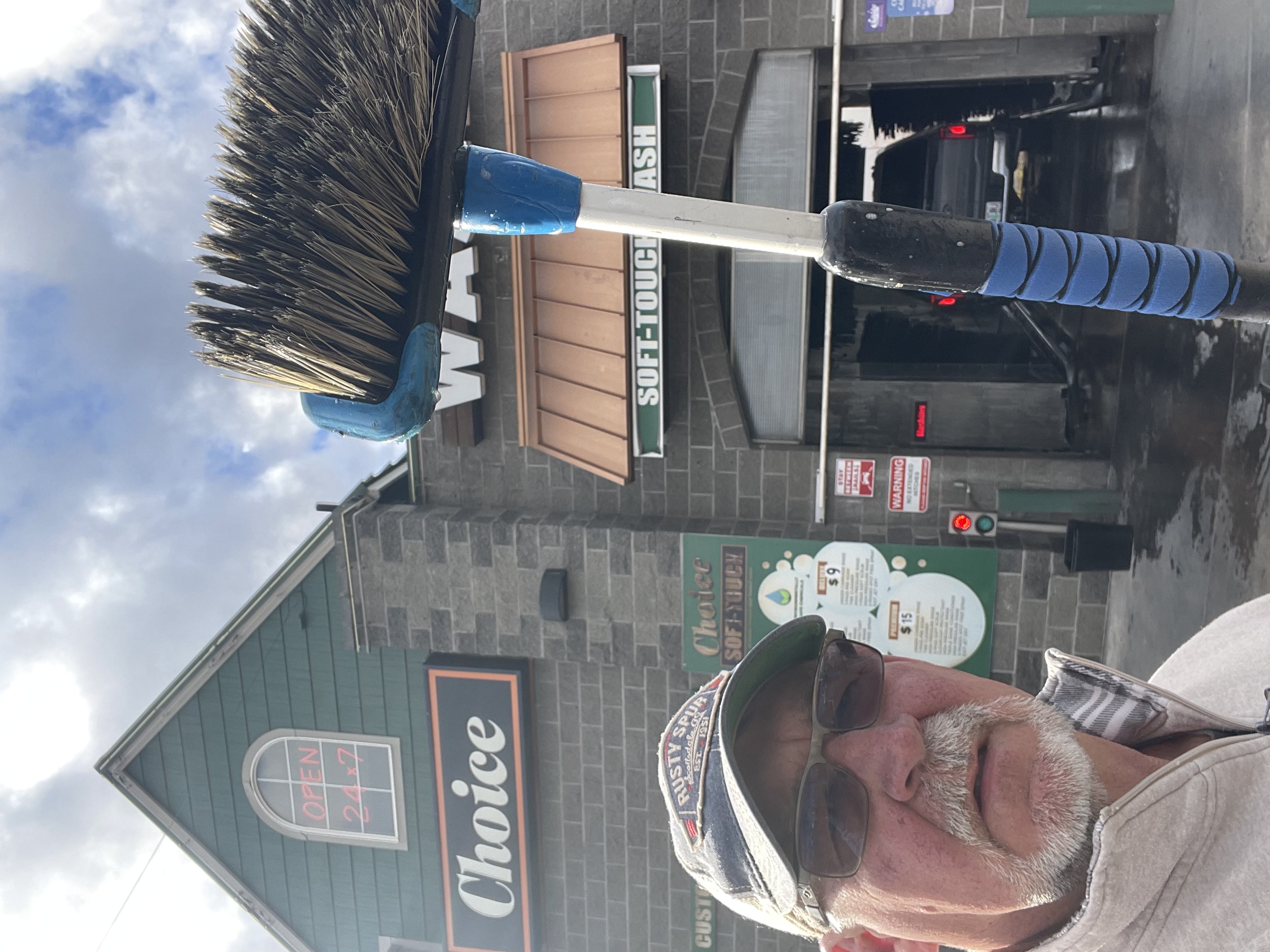 Owner of Choice Car Wash, standing in front of the car wash building with brush in hand