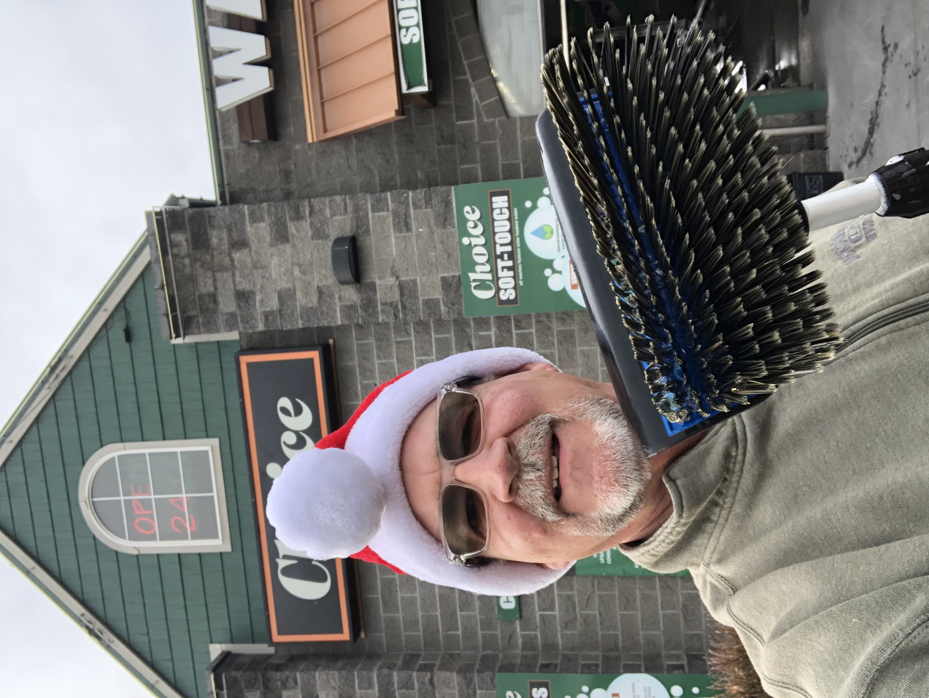 Owner of Choice Car Wash, standing in front of the car wash building with Christmas hat and brush